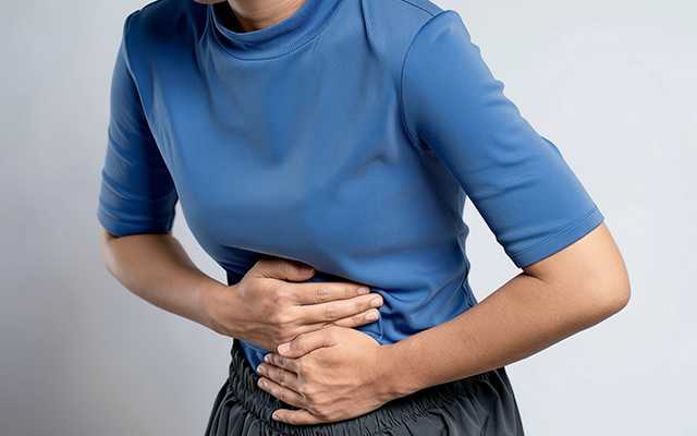 A woman clutching her abdomen in pain, possibly experiencing discomfort related to her abdominal area or digestive issues.